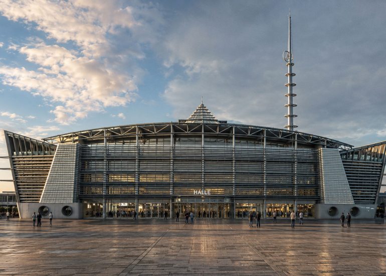 Rheinhafen Exhibition Center Karlsruhe, frontal exterior with louvered facade, roof trusses, and broad plaza.